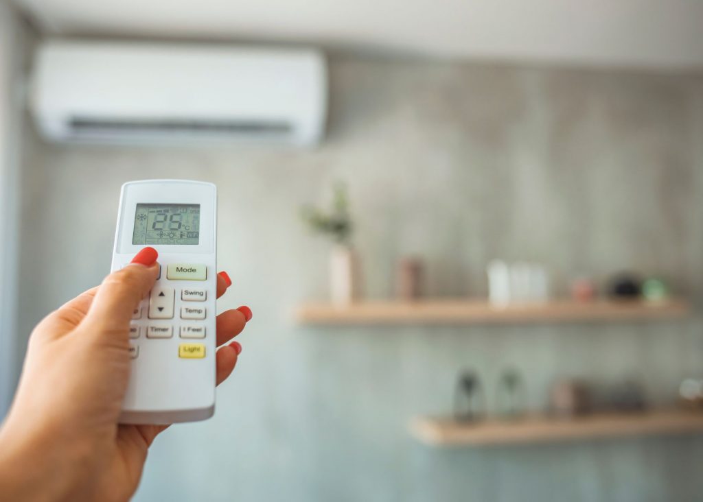 Split air conditioning unit on the wall with hand holding remote control with cool temperature in the foreground
