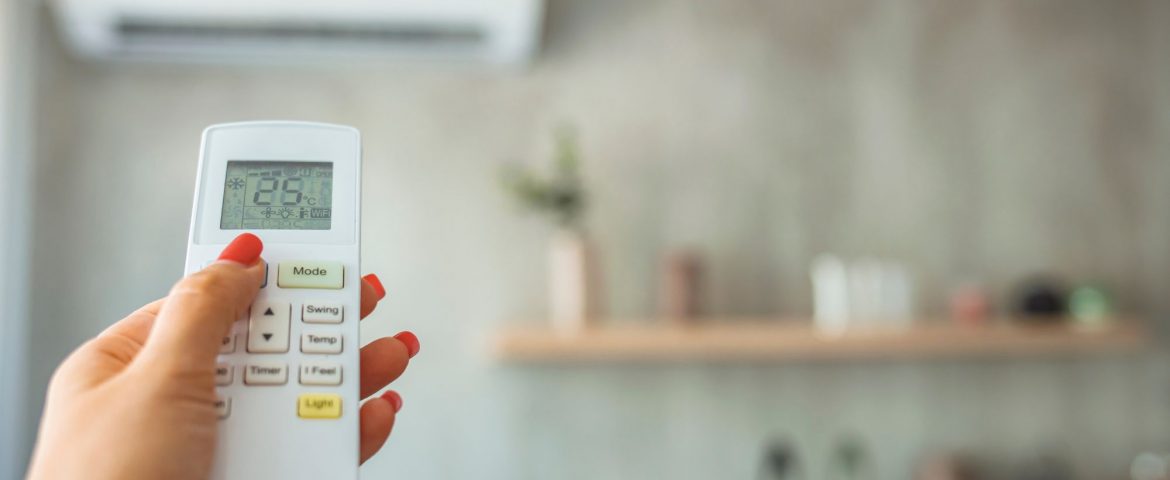 Split air conditioning unit on the wall with hand holding remote control with cool temperature in the foreground