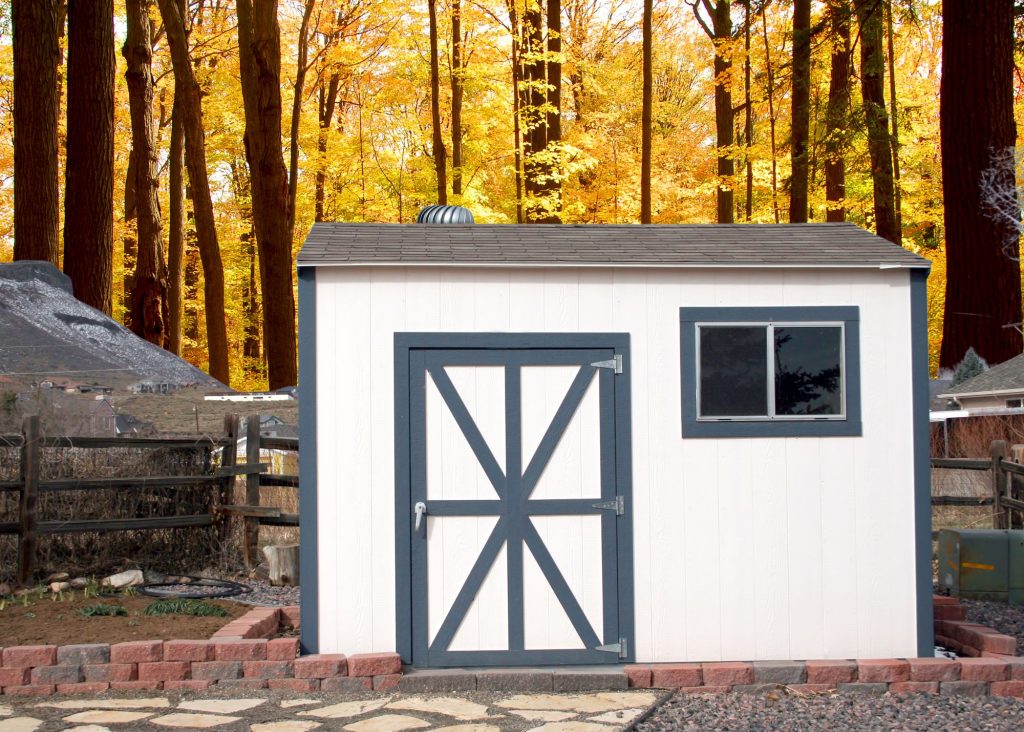 Organized garden shed by split rail fence and autumn foliage