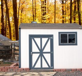 Organized garden shed by split rail fence and autumn foliage