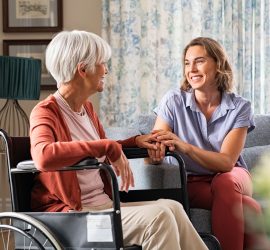 Mother in wheelchair with daughter holding her hand in living room